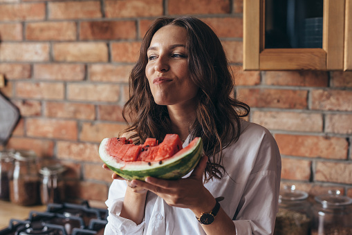 Woman at home eating watermelon in the kitchen.