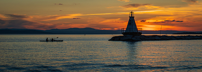 kayakers approaching the Lake Champlain breakwater's lighthouse with a sea bird perched on the top at sunset