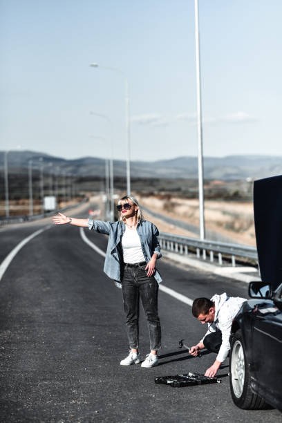 istock Female Calling For Help While Boyfriend Tries To Fix Broken Car On Highway 1325790014