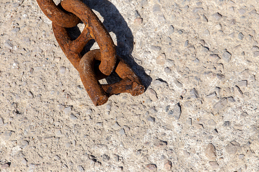 Strong iron mooring chain broken in half, lying on concrete under mid day sun, with copy space.