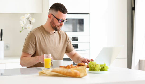 istock Young focused handsome man working remotely on laptop in modern kitchen at home 1325802753