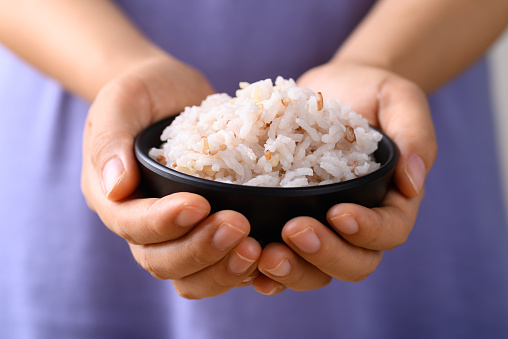 Organic Thai highland cooked brown rice in a bowl holding by woman hand (Cargo rice, Loonzain rice or Husked rice), Healthy food