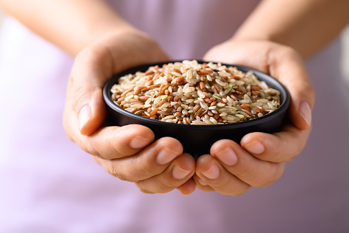 Organic Thai highland brown rice grain in a bowl holding by woman hand (Cargo rice, Loonzain rice or Husked rice), Healthy food