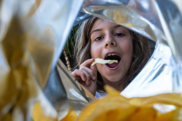 un niño comiendo patatas fritas de un paquete. - malnourished fotografías e imágenes de stock