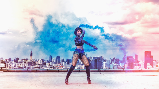 woman dancer showing modern dance performance with color smoke on rofftop of highrise building in city