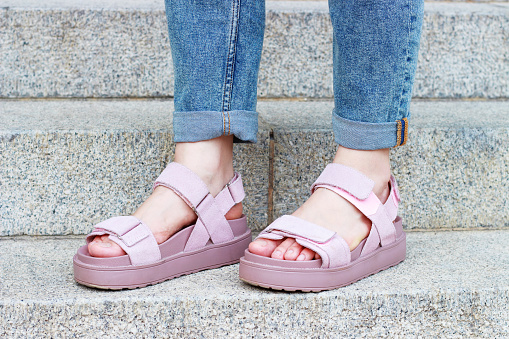 Female feet in pink sandals on on a concrete staircase background close-up.
