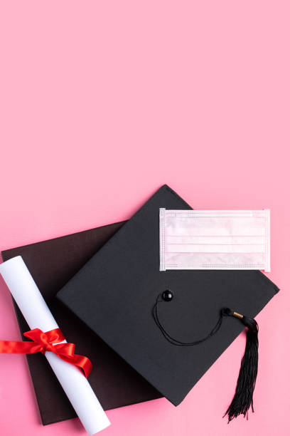 istock Graduation academic cap with diploma and mask isolated on pink table background. 1325828550