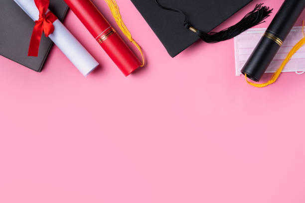 istock Graduation academic cap with diploma and mask isolated on pink table background. 1325828598