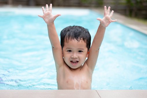 Portrait of asian little boy looking at camera and smiling while playing water in the swimming pool. Summer activity and childhood lifestyle concept.