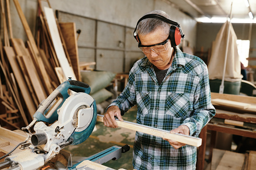 Serious senior carpenter measuring wooden plank before cutting it with circular saw