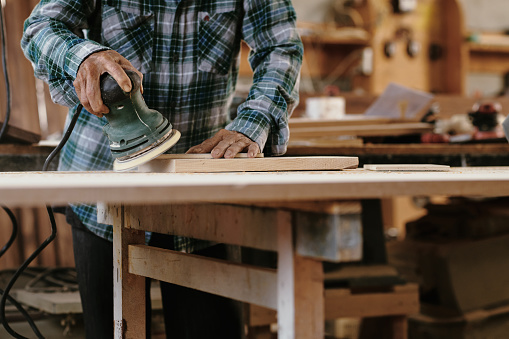 Hands of senior experienced carpenter sanding edges of wooden board
