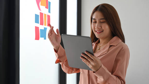 istock Businesswoman using digital tablet and reading sticky notes on glass wall. 1325840992
