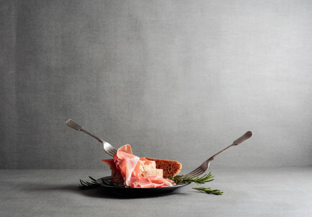 Prosciutto with bread and rosemary on a black plate.