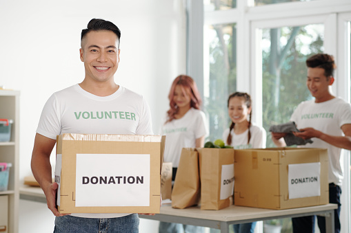 Portrait of happy young man working in charitable foundation and packing donation boxes for food bank