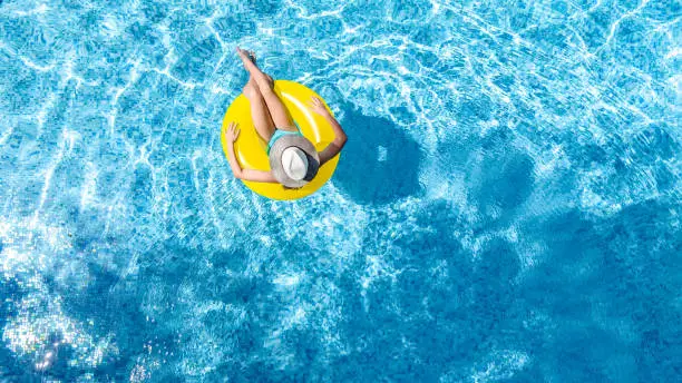 Photo of Active young girl in swimming pool aerial top view from above, child relaxes and swims on inflatable ring donut and has fun in water on family vacation, tropical holiday resort