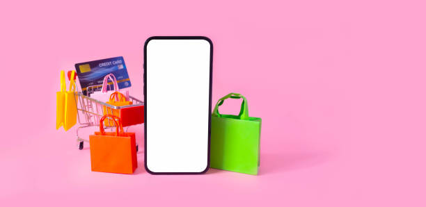 Shopping and payment with smartphone white screen and shopping bag, credit card in cart on pink background.Consumers can buy everything from online stores using a smart device connects to internet. compras y pago con pantalla blanca de smartphone y bolsa de la compra, tarjeta de crédito en carrito sobre fondo rosa. los consumidores pueden comprar todo en las tiendas en línea utilizando un dispositivo inteligente que se conecta a internet.