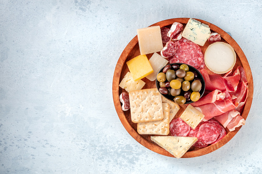 Cold meat and cheese board, shot from above with copy space. Prosciutto di Parma ham, blue cheese, olives and crackers. Gourmet antipasti