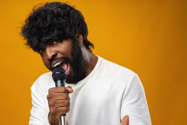 istock Young bearded african american man singing in microphone against yellow background 1325850559