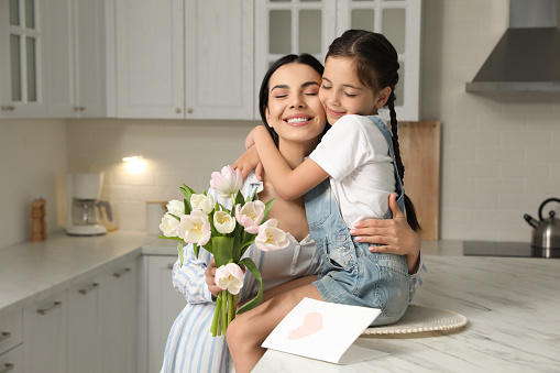 Little daughter congratulating her mom in kitchen at home. Happy Mother's Day