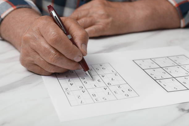 istock Senior man solving sudoku puzzle at white marble table, closeup 1325852969