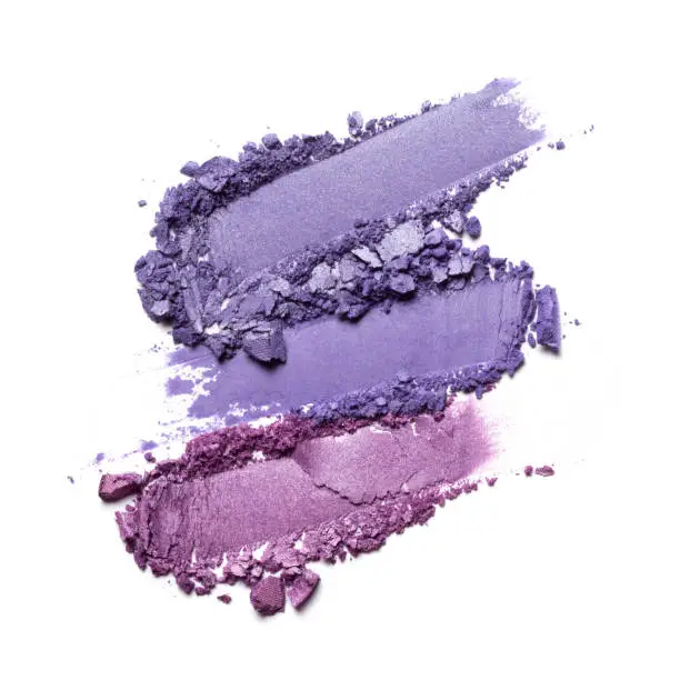 Flat lay of brush strokes. Broken shiny bright purple eyeshadow as samples of cosmetic beauty products isolated on white background