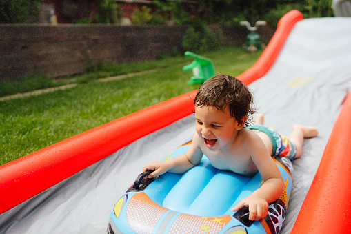 Photo of a little boy having fun on the water slide in the backyard
