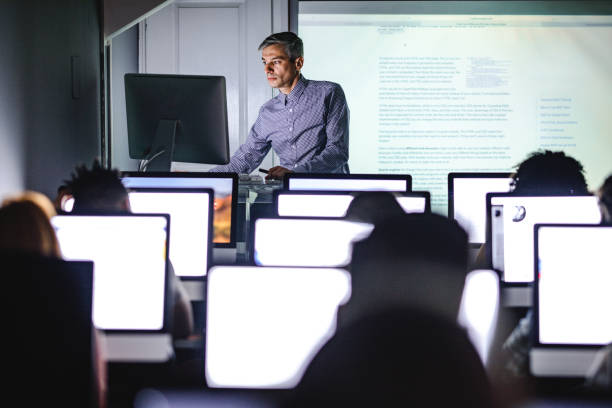 istock Mid adult professor teaching a lecture from desktop PC at computer lab. 1325855541