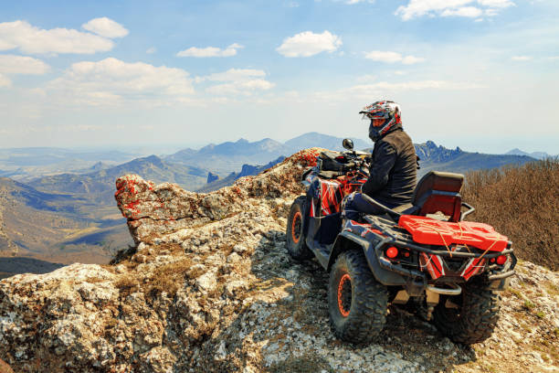 hombre con casco sentado en quad atv en las montañas - off road vehicle fotos fotografías e imágenes de stock