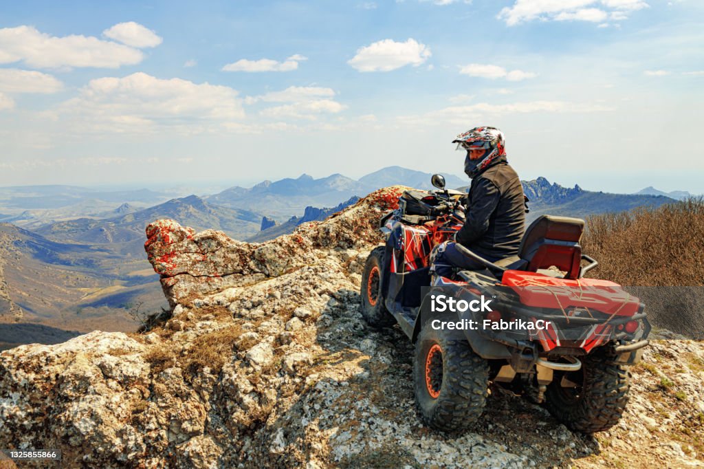 Man in helmet sitting on ATV quad bike in mountains Man in helmet sitting on ATV quad bike in mountains on race Off-Road Vehicle Stock Photo