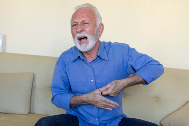 älterer mann mit grauen haaren und bart fühlt schmerzen in der hand und fühlt sich unzufrieden und verzweifelt. - arthritis senior adult rheumatoid arthritis sadness stock-fotos und bilder