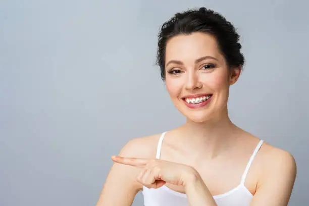 Young woman with braces on teeth laughing and points with his hand to the copy space.