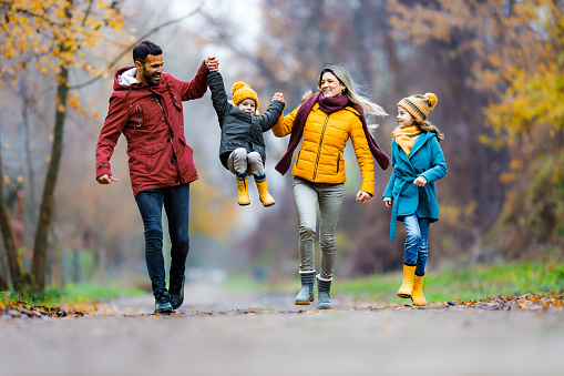 Young cheerful family having fun in autumn day at the park. Parents are swinging their small son. Copy space.