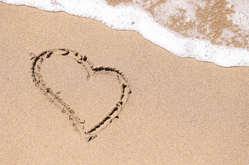 Drawn heart on wet sand next to sea. Romantic travel to the sea concept
