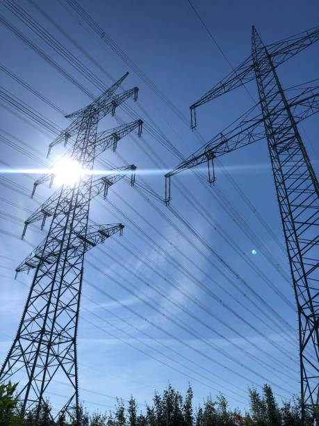 istock Electricity pylons against a blue sky and sun 1325864483