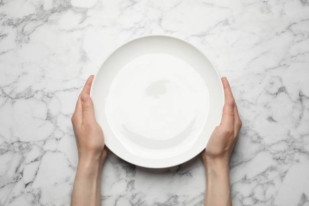 istock Woman with empty plate at white marble table, top view 1325864536