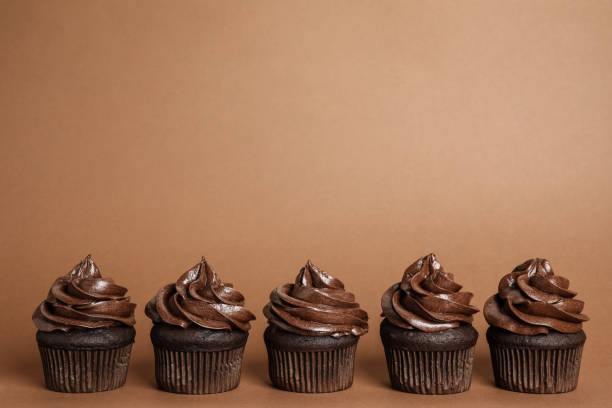istock Delicious chocolate cupcakes with cream on brown background. Space for text 1325864595