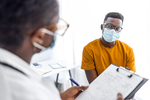 Black female doctor communicating with a patient while wearing protective face mask during medical appointment.