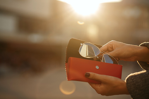 Closeup shot of female hand opening red glasses case at the background of sun. Space for text