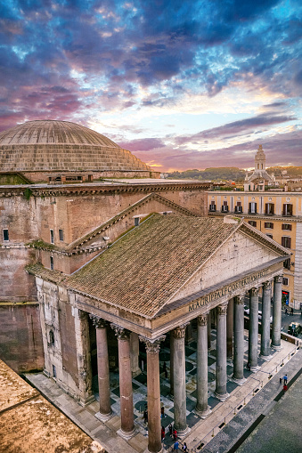 The majestic Roman Pantheon at sunset from the rooftops of the historic heart of Rome. The famous Pantheon with its dome and colonnade is one of the best preserved Roman structures in the Eternal City. This temple was built in 27 BC. by the Consul Marco Vispanio Agrippa for the emperor Augustus and dedicated to all the Roman divinities. Currently the Pantheon is a Catholic church and inside there are the tombs of some members of the Italian royal family and the remains of the great Renaissance artist Raffaello Sanzio (Raffaello). Image in high definition format.