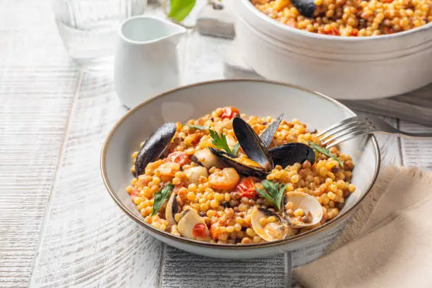 Italian pasta. Fregula with seafood on a white wood surface.