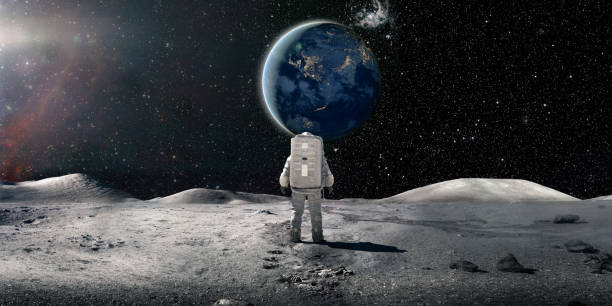 Lone Astronaut In Spacesuit Standing On The Moon Looking At The Distant Earth A single astronaut viewed from behind, standing and looking at the sun rising over a distant plant earth surrounded by distant stars and galaxies. The astronaut is wearing a conventional white spacesuit with backpack. Earth image from NASA: https://eoimages.gsfc.nasa.gov/images/imagerecords/79000/79790/city_lights_asia_night_8k.tif moon surface stock pictures, royalty-free photos & images