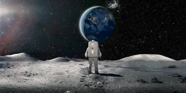 Photo of Lone Astronaut In Spacesuit Standing On The Moon Looking At The Distant Earth