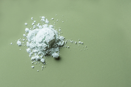 Alginate mask powder or green cosmetic clay bentonite powder, dry body wrap sample texture on green background, copy space. Skin care, body care concept.