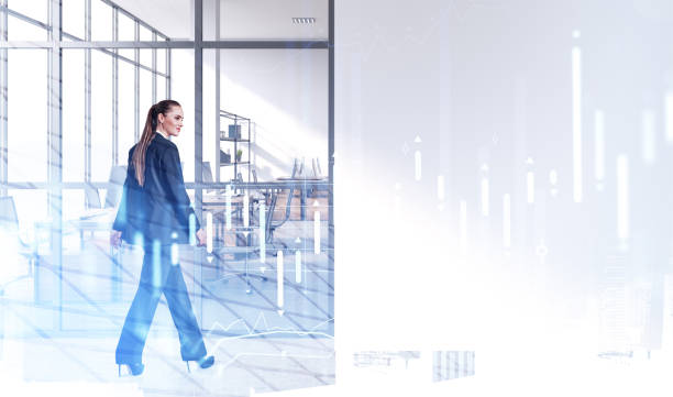 istock Young businesswoman walking along office open space. Double exposure. Workspaces on background. Forex chart over 1325873197