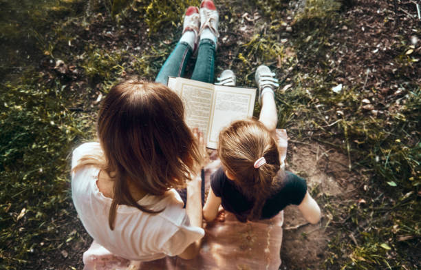 mamma e figlia in una soleggiata giornata estiva nel parco leggono un libro. un posto dove rilassarsi, un momento di madre e figlia. aria fresca in natura - child reading mother book foto e immagini stock