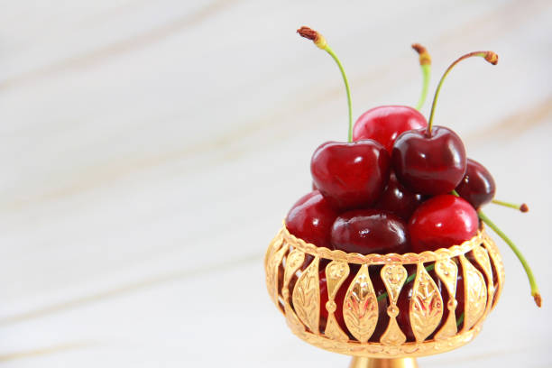 Stock photo shows a closeup of two pairs of red cherries with stems isolated on a clean background, showcasing their vibrant color and glossy texture. These juicy summer fruits highlight natural freshness and ripeness