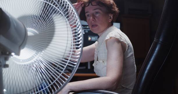 istock Woman is trying to work at the desktop computer at home, suffering from hot weather and using electric fan 1325878028