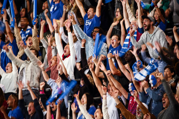 Large number of spectators on a match clapping, smiling and cheering for the blue team.