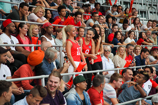 Three women in red standing and smiling . Many spectators on a stadium.