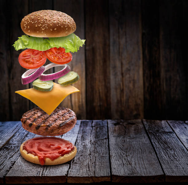 istock Burger layered ingredients as explosion flying open bun on rustic wooden table 1325880512